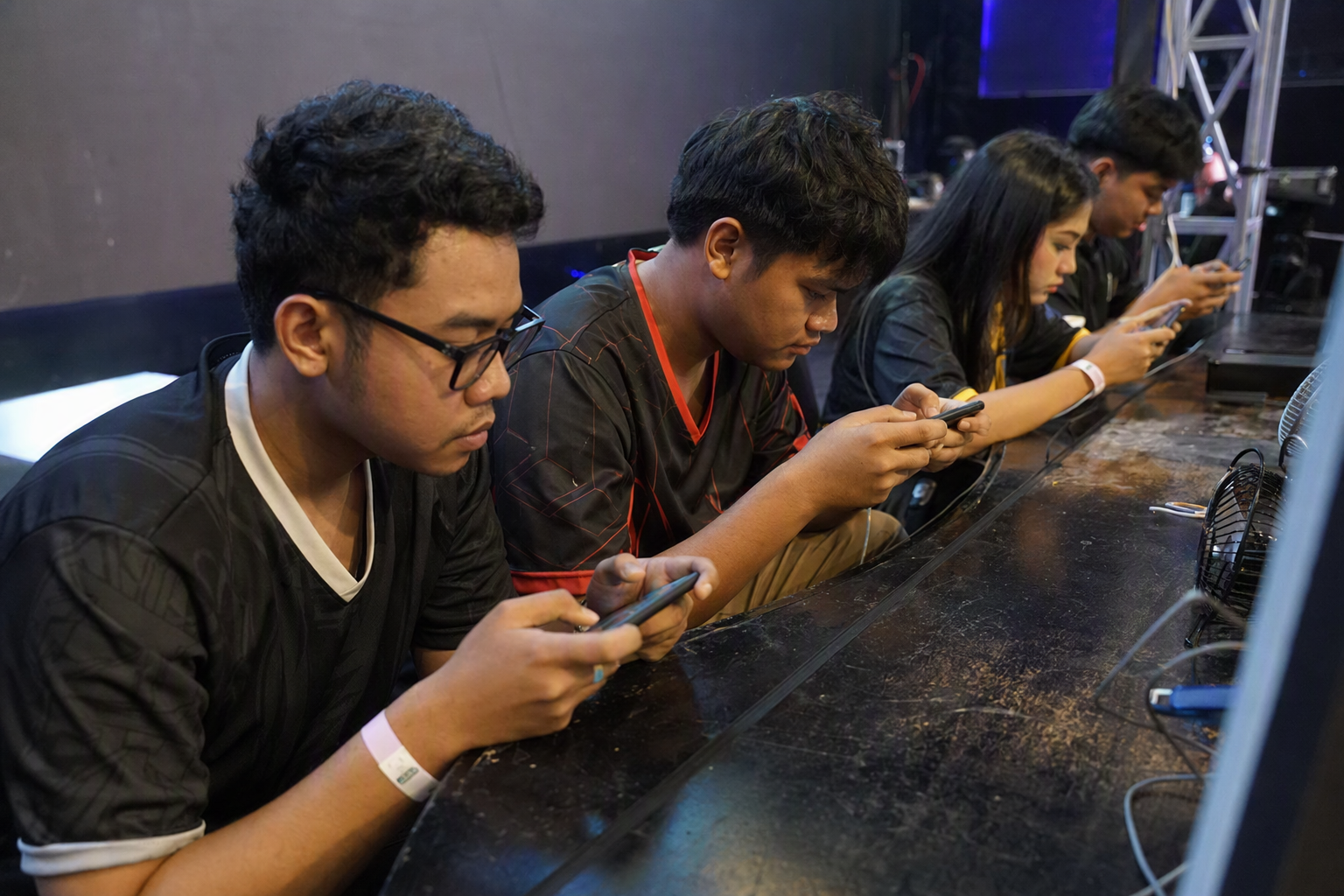 Diverse community competitors holding mobile phones at a professionally lit independent esports event